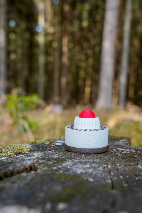 Schwarzwälder Kirschtorten-Klicker Schwarzwälder Kirschtorten-Klicker auf einem Holzstamm vor einem Waldhintergrund
